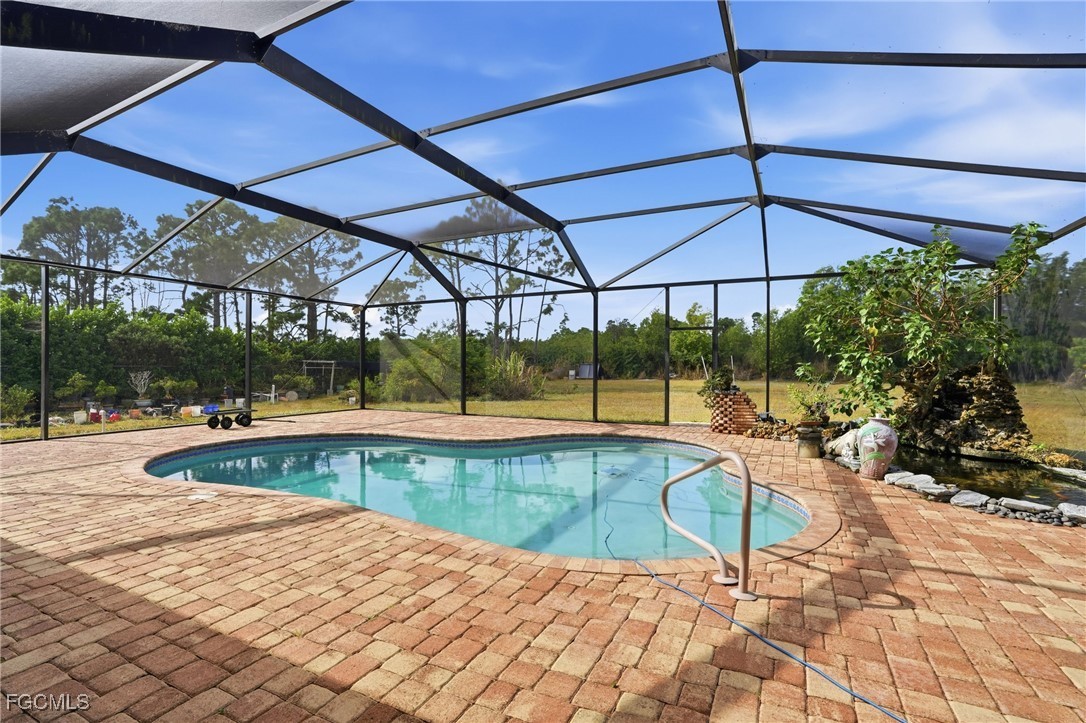 Screened lanai over a freeform paver pool deck, looking out across the open backyard toward the treeline