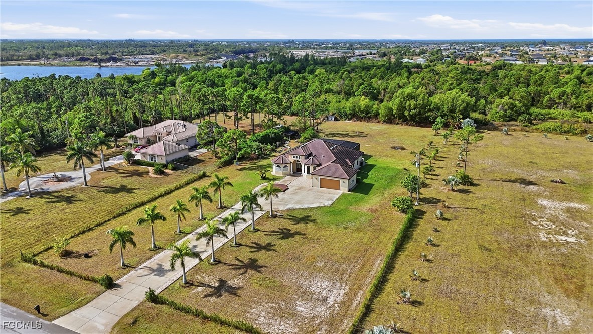Aerial daytime view of the 1.81-acre property at 3816 NW 32nd Pl with a palm-lined driveway leading to the Mediterranean villa, distant waterway behind the property