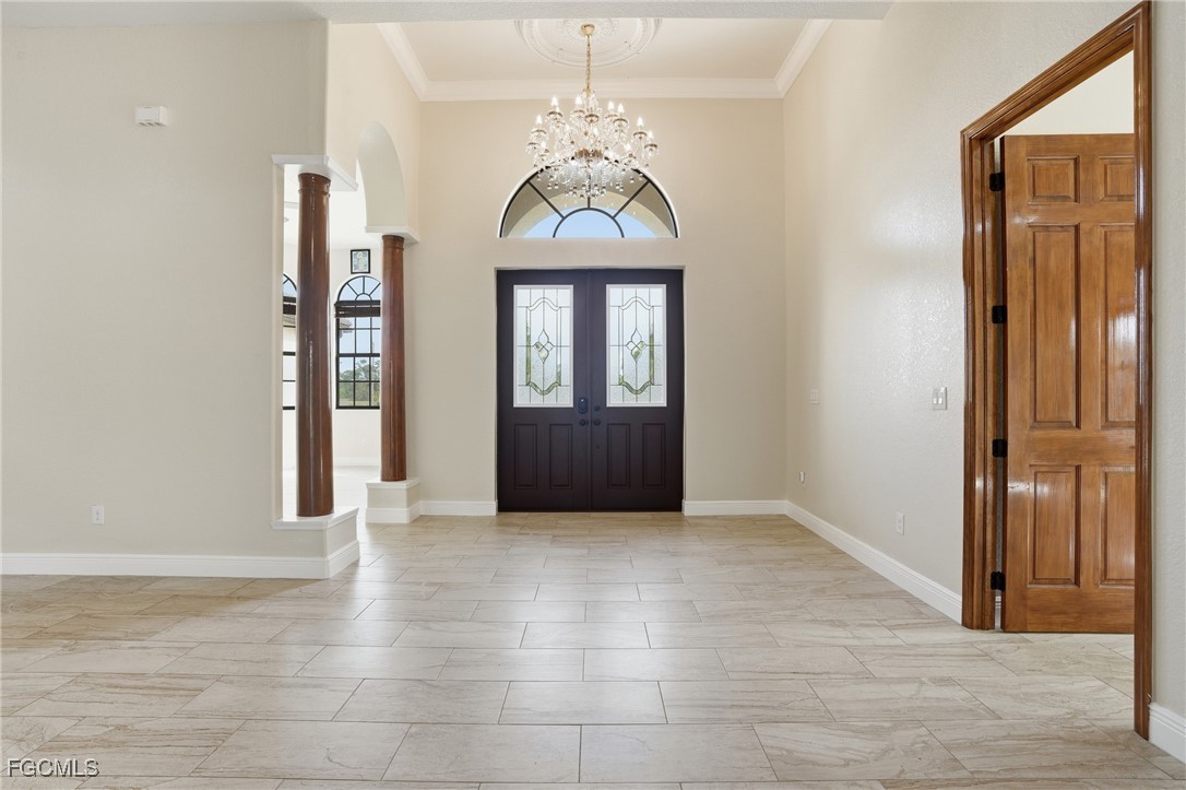 Two-story foyer with a crystal chandelier, double doors with stained-glass insets, and ornamental columns on travertine tile