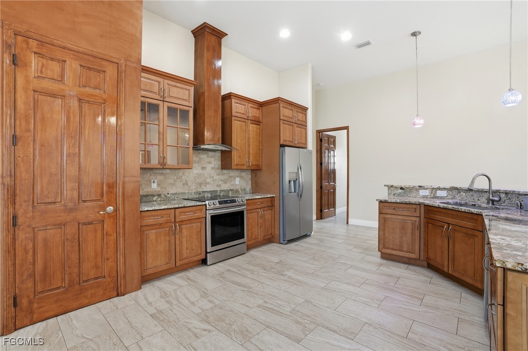 Kitchen detail showing stainless range, stone-tile backsplash, and a tall maple pantry door beside the cooktop