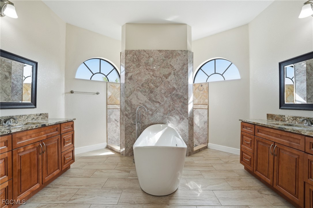 Primary bath with a freestanding soaking tub centered between dual maple vanities with stone counters and arched windows above