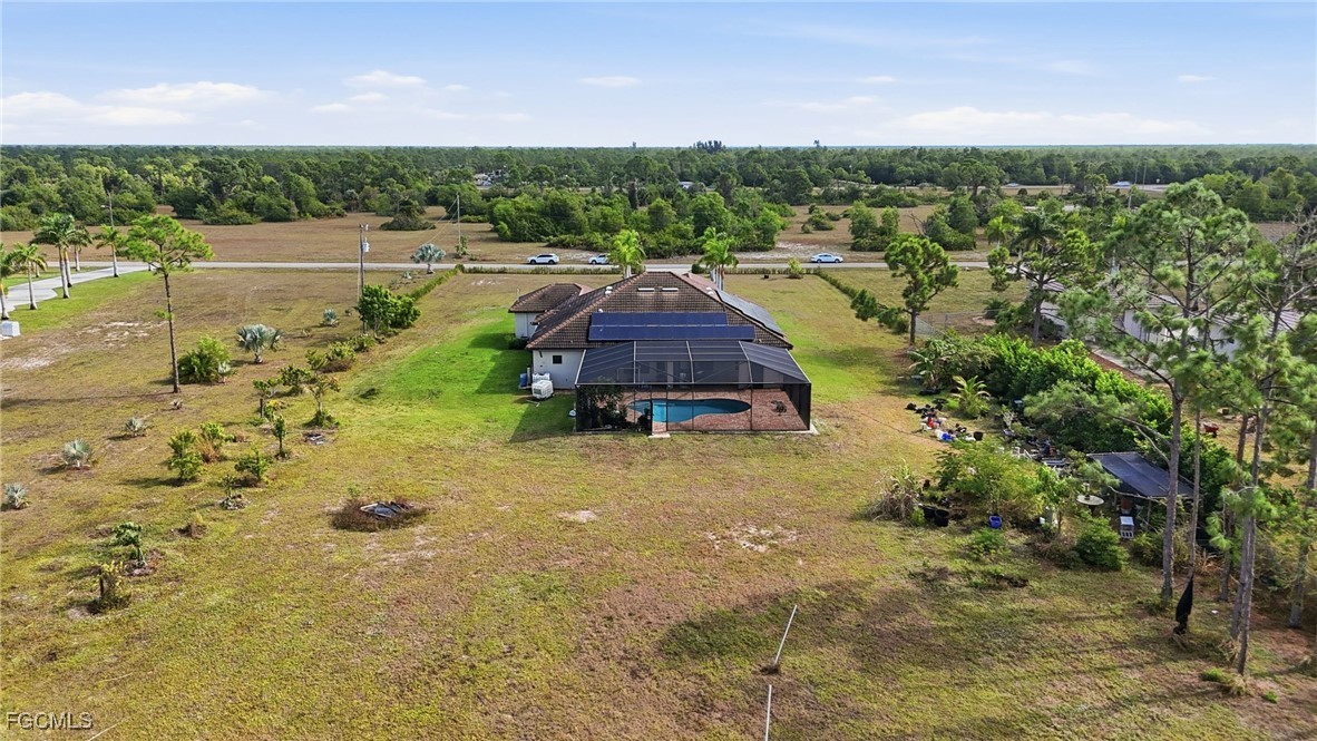Aerial rear view showing the screened pool enclosure, solar panels on the tile roof, and the depth of the back lot leading to the treeline