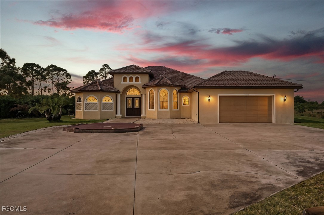 Twilight exterior of the Mediterranean villa at 3816 NW 32nd Pl, Cape Coral, with a tile roof, arched windows, and a pink dusk sky